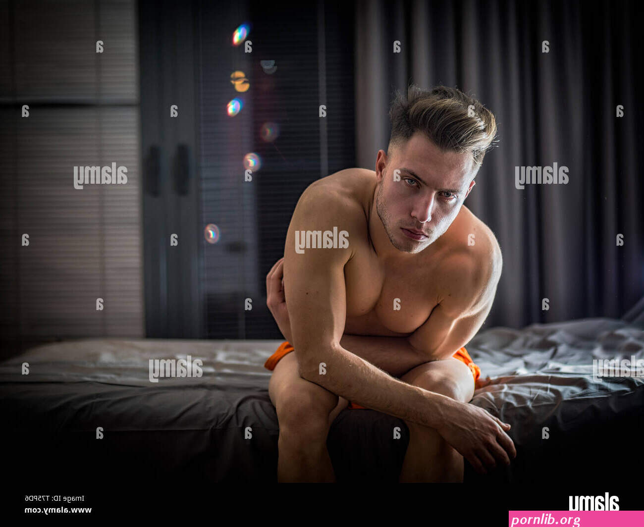 Shirtless naked sexy male model sitting on bed Stock Photo