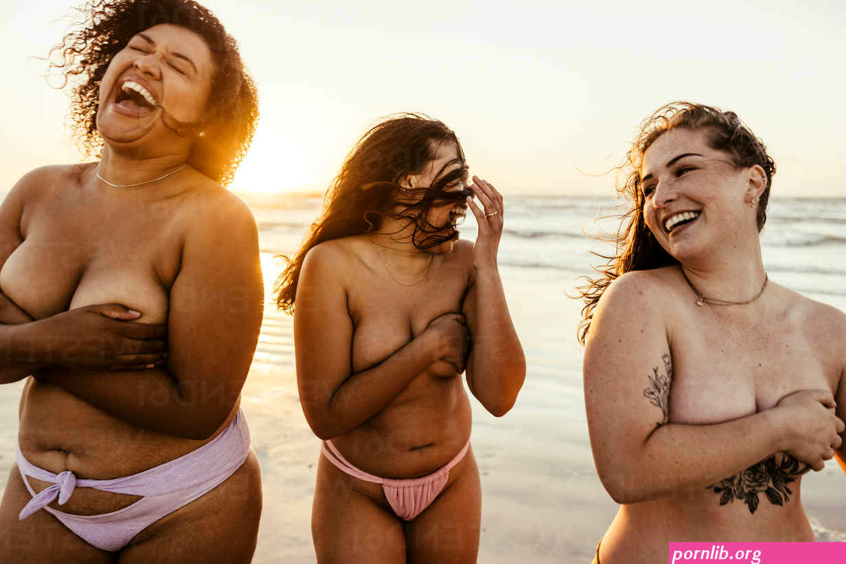 Topless women laughing cheerfully at the beach. Carefree female friends having fun and enjoying themselves in bikini bottoms. Group of girlfriends enjoying their summer vacation together. stock photo